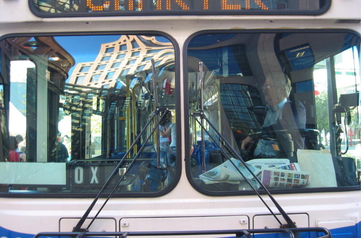 Extreme close-up of the front of a TransLink bus; tall buildings reflected in the windshield