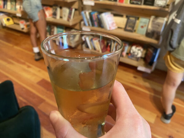 Hand holding a glass of beer with bookshelves in soft focus in the background